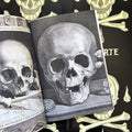 Inside pages of 'Muerte', featuring a black and white etching of a skull missing many teeth and looking straight on.