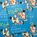 Front cover of, 'Animals by Kuniyoshi', featuring a pack of koi fish walking together, holding fans and holding each others fins over a blue background