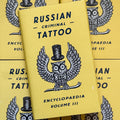 Front cover of, 'Russian Criminal Tattoo Encyclopaedia Vol. 3', featuring a yellow cover with a black and white owl over it wearing a top hat and a bowtie