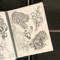 Inside pages of The Black Book featuring line drawings of cheetah heads, an anatomical heart and dagger, a simple cat, and a man sitting on a tree stump.