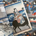Inside pages of Hiroshige featuring a woodcut print of a warrior on a horse, with the sea in the baclkground.