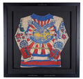 Auction item from "The Tattoo Catalogue 2026: Tattoo, Circus, Sideshow, and Curiosities". Framed Lyle Tuttle tattoo body shirt from 1972 with designs by Bert Grimm. Long-sleeve printed shirt depicting a full traditional back piece: a spread-winged eagle over a "Duel in the Sun" banner with sunburst rays, flanked by roses, spiderwebs, butterflies, and pin-up figures on the sleeves, in red, blue, and cream.