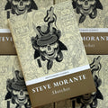 Front cover of Steve Morante's Sketches featuring line drawings of Japanese designs on a light yellow background and a black and grey painting of a samurai skull in the foreground. Simple and bold white lettering is used for the title.