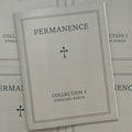 Front cover of, 'Permanence', featuring a grey soft cover book with a black mini cross in the center