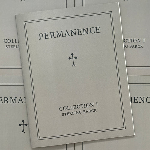 Front cover of, 'Permanence', featuring a grey soft cover book with a black mini cross in the center
