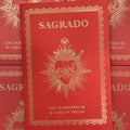 Front cover of 'Sagrado' by Carlos Truan and Zac Scheinbaum featuring a gold embossed sacred heart illustration, along with the title, authors, and a decorated frame, all on a red background.