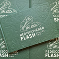 Front cover of Stoney St. Clair 'Rediscovered flash Vol. 2', featuring a green hardcover with flash prints of a cobra, a frog, flowers, a spiderweb heart, and more.