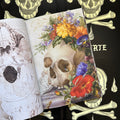 Inside pages of 'Muerte', featuring a realistic oil painting of a skull with colorful flowers around it, sheets of music, and a butterfly and snail.