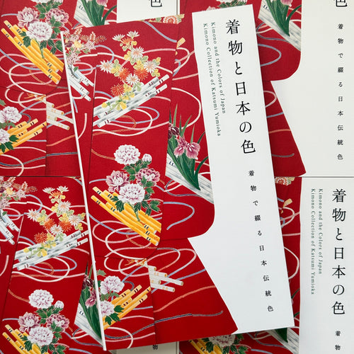 Front cover of, 'Kimono and the Colors of Japan', featuring a red Kimono on the cover with light pink peony pattern over bamboo rods