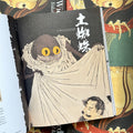 Inside pages of, 'Something Wicked from Japan', featuring a giant spider with a cloak on, trying to cover a Japanese mans head, with Japanese characters in the background