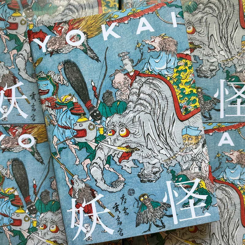 Front cover of, 'Yokai', featuring many Yokai marching together, some on top of an elephant, some holding weapons like bows and spears, and some blowing horns, all over a blue background