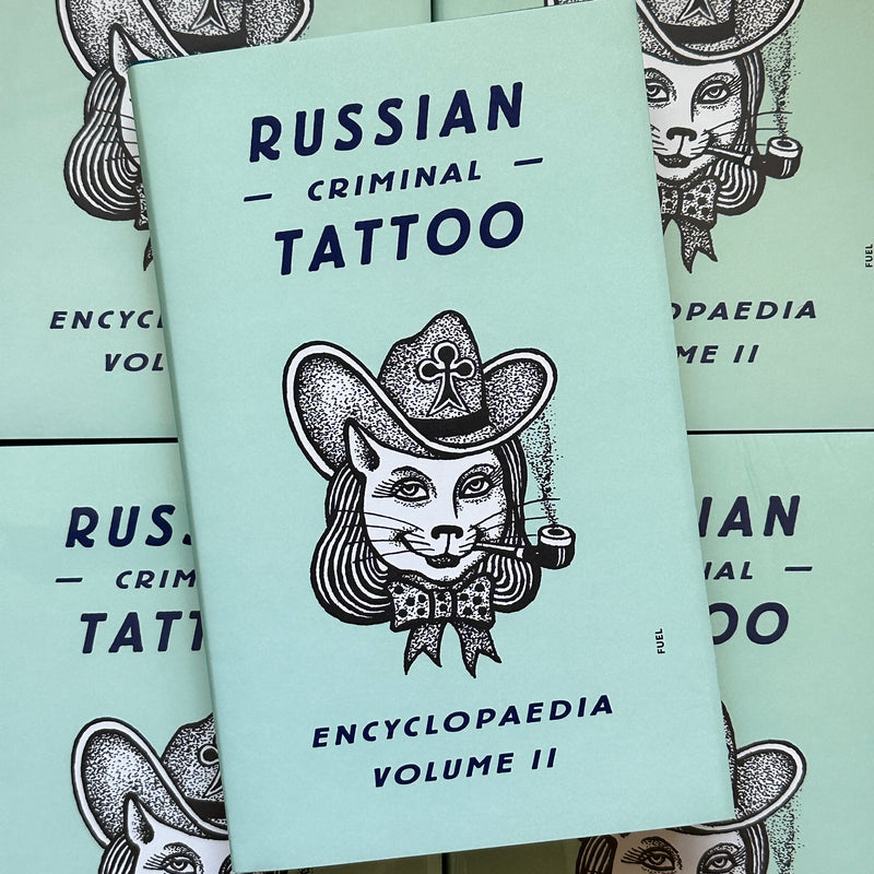 Front cover of, 'Russian Criminal Tattoo Encyclopaedia Vol. 2', featuring a cat with hair smoking a pipe, with a cowboy hat and a bowtie on, over a mint green background