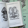 Inside pages of, 'Russian Criminal Tattoo Encyclopaedia Vol. 2', featuring a devil sitting down, with a skull on it's penis, holding up a bell and a glass bottle in it's hands on either side, with russian text above and below it