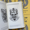 Inside pages of, 'Russian Criminal Tattoo Encyclopaedia Vol. 3', featuring a horned skull with stars in it's eyes, facial hair, and barbed wire wrapped around it with a lookout post on it's head and russian text below it