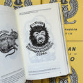 Inside pages of, 'Russian Criminal Tattoo Encyclopaedia Vol. 3', featuring a horned monster with it's mouth open and eyes squinting, with Russian text above and below it