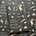Front cover of, 'Cats by Kuniyoshi', featuring cats dancing, licking their paws, dragging things, etc scattered on the cover of a black background