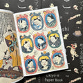 Inside pages of, 'Cats by Kuniyoshi', featuring 9 oval frames side by side with portraits of cats wearing robes inside of them 