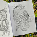 Inside pages of The Dragon Sketchbook by Erik Rieth, a line drawings and sketches tattoo book, featuring a a detailed full-body dragon with wings and a spiky tail.