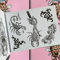 Inside pages of Tattooing Flash Book by Frank Ball featuring tribal designs and three scorpions. One scorpion surrounded by stars, one scorpion holding a knife with its tail, and one scorpion adorned with tribal flames.
