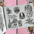 Inside pages of Tattooing Flash Book by Frank Ball featuring biker imagery, including a lady posing with a bike, the Harley-Davidson logo, a tire with wings, a winged skeleton riding a winged coffin shaped like a motorcycle, and others. 