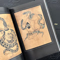 Inside pages of Essential Works From the Studio of George Burchett featuring a vintage illustration of a skull with two snakes going through it.