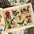 Inside pages of Nate Moretti - Traditional Tattoo Flash featuring a range of colorful flash which includes birds, a dog, and a hula dancer next to a giant flower.