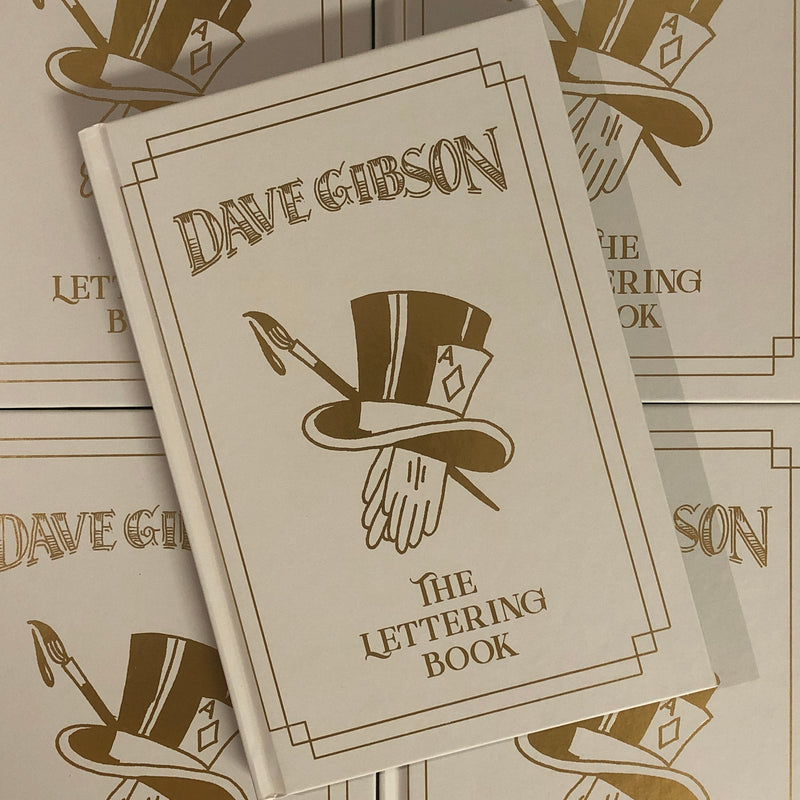 Front cover of Dave Gibson - The Lettering Book featuring gold lettering and a magicians hat, gloves, an Ace card, and a paint brush as the magic wand.  A simple border of two rectangles intersecting at the corners surrounds the lettering and imagery.